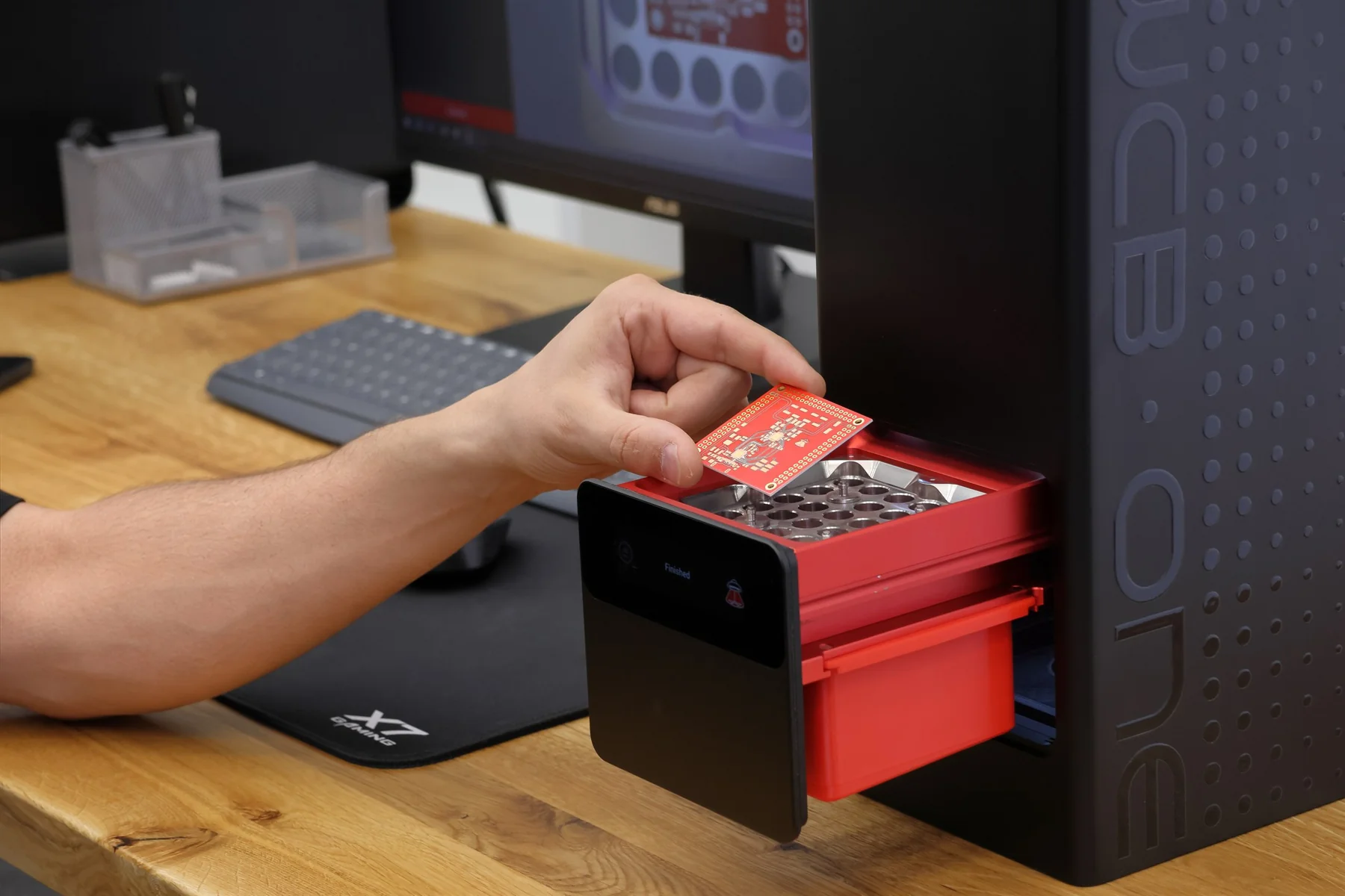An engineer removes a finished PCB from the PewCB One work tray